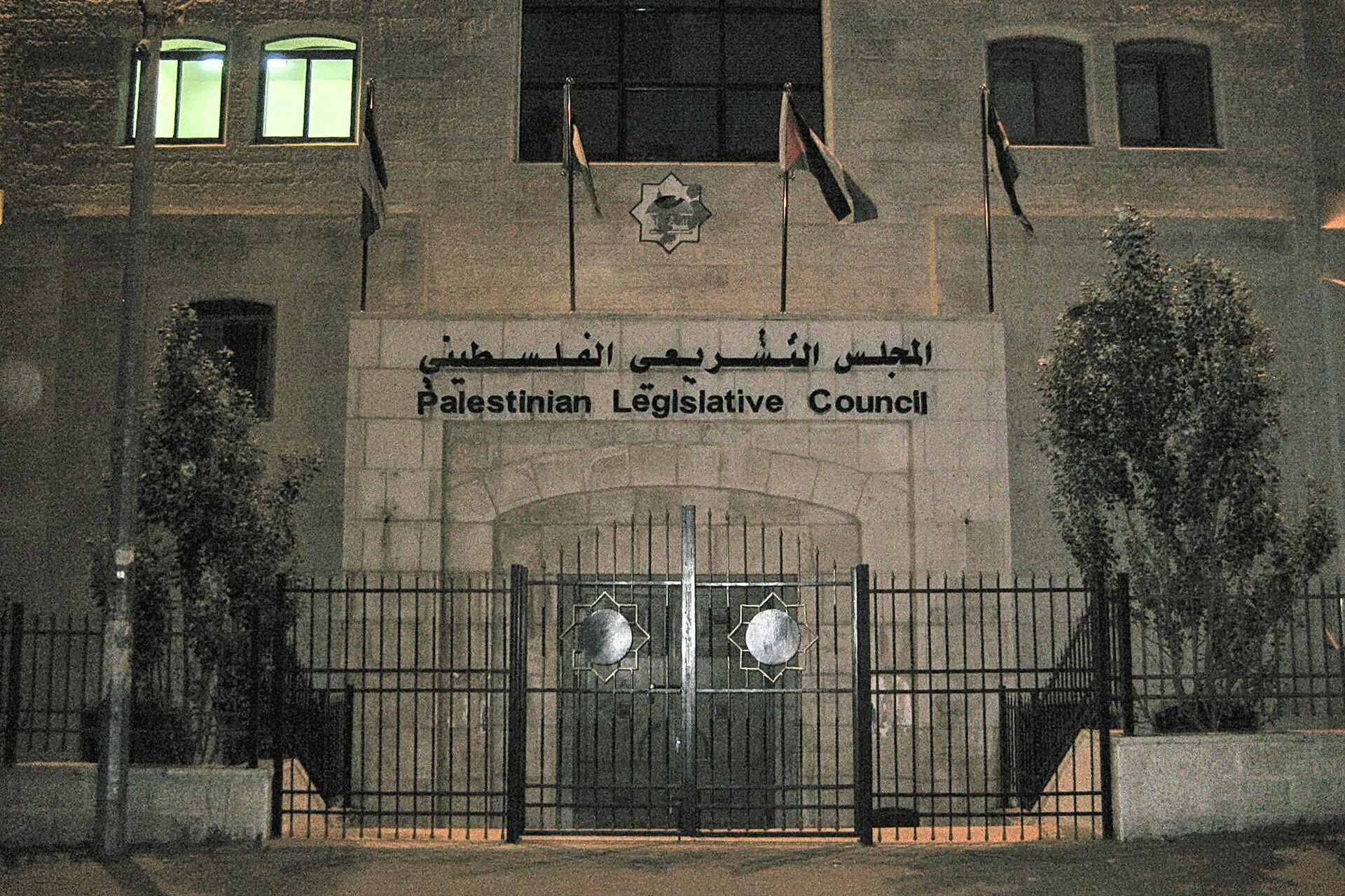 Stone facade of the Legislative Council building at night, its iron gate closed and flags above the entrance